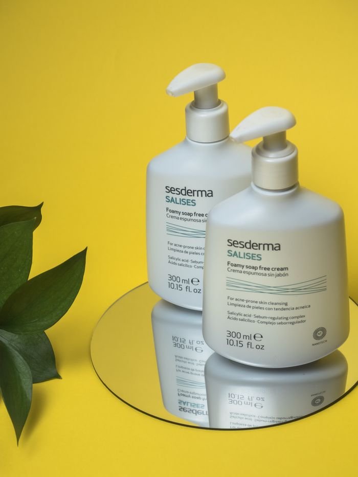 Close-up of skincare foamy soap-free cream bottles on a mirror with a yellow backdrop.