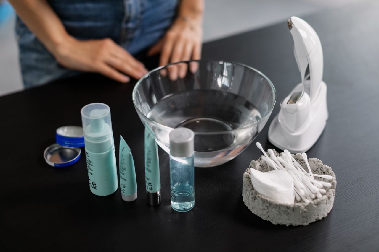 Flat lay of skincare products, tools, and a glass bowl on a black surface for beauty care routines.